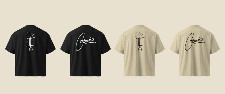 the backs of four foundation tees laid flat, black and stone, printed with the face drawing and the cosmo’s signature